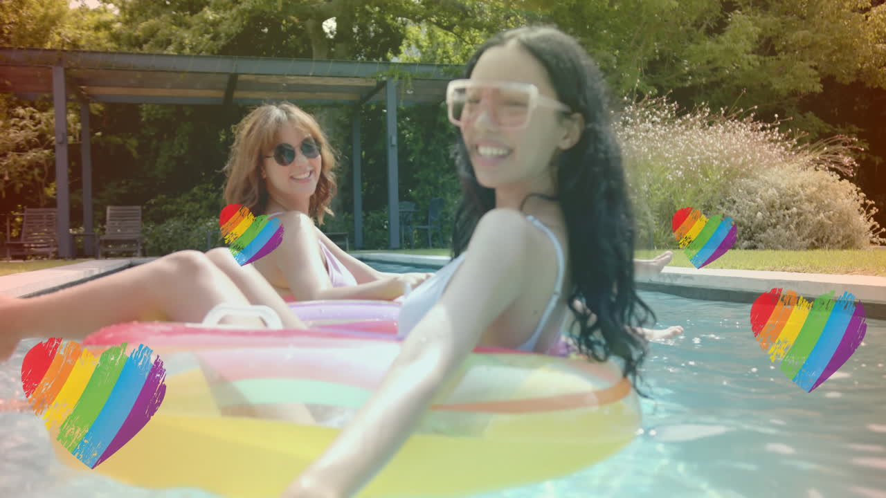 무지개 심장 애니메이션으로 수영장에서 웃는 여성들이 그들을 둘러싸고 떠다니고 있습니다.