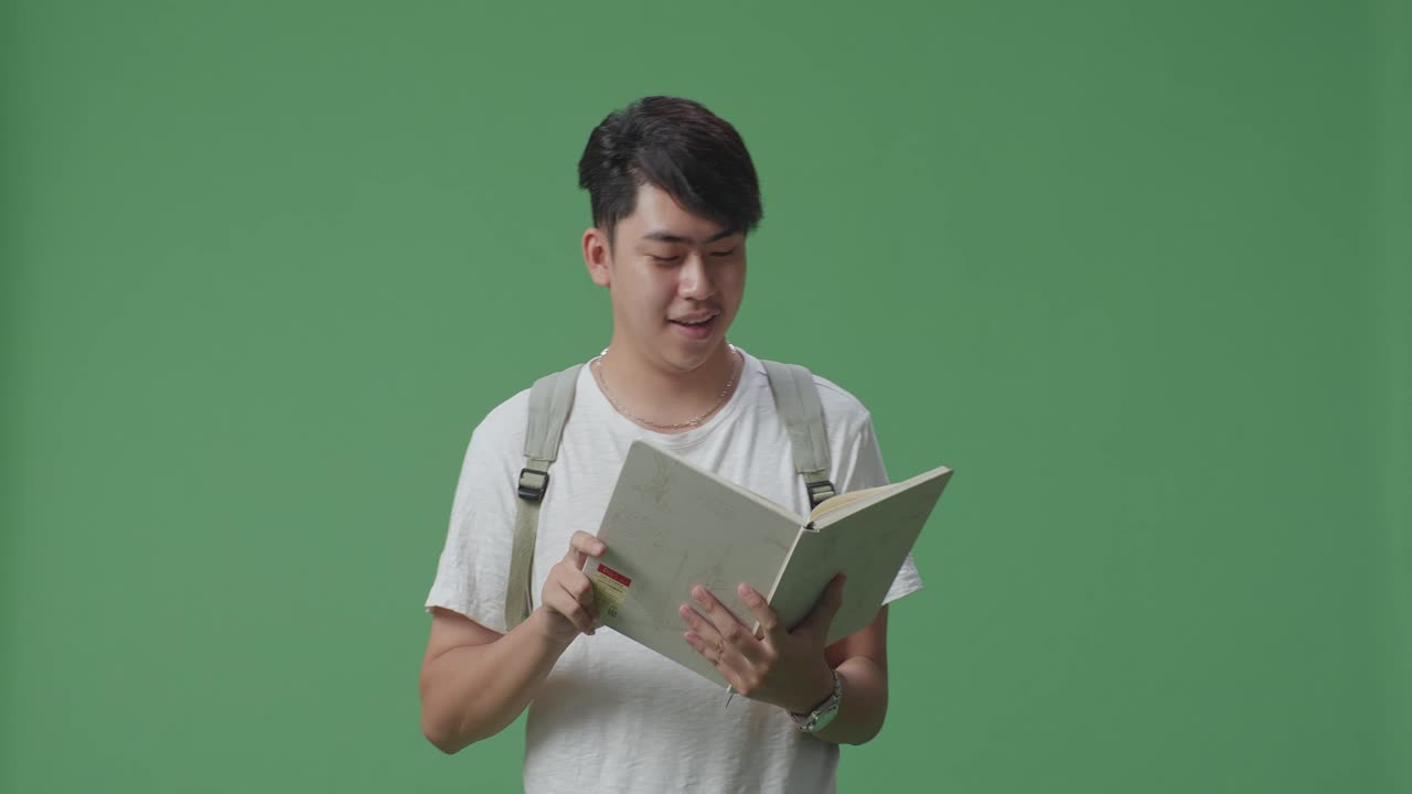 아시아 남성 학생이 책을 읽고 녹색 스크린 스튜디오에서 고 있습니다.