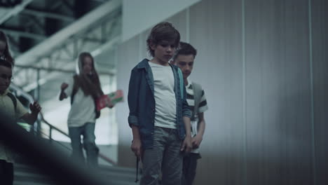 sad little guy standing alone on school stairs. pupils running downstairs.