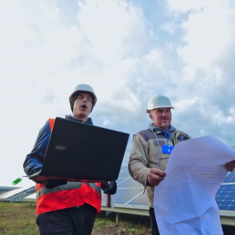 workers in hard hat on the solar farm. engineers talk about solar panels installation. technicians with a laptop and project discuss the construction of new ecological station.