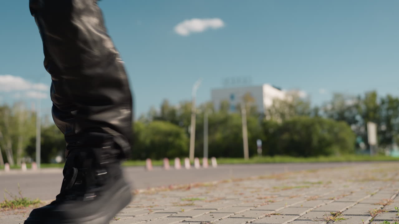 Biker woman walking on pavement under clear sky wearing sunglass confidently swinging jacket over shoulder with relaxed stride urban background of building trees and parked cars