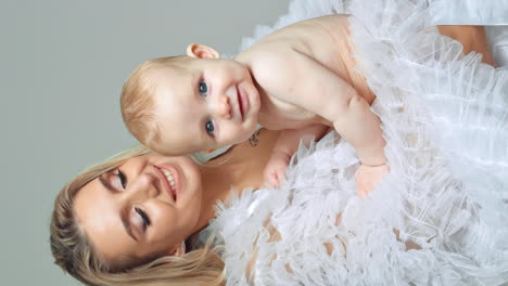 portrait of a beautiful caucasian woman with baby in hands. adorable grey-eyed child looking at camera. white backdrop. vertical screen.