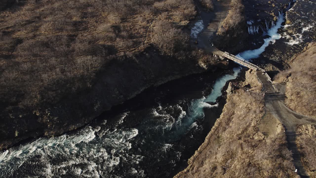 impresionante puente sobre un río salvaje y una cascada en un vasto paisaje volcánico