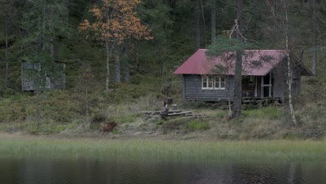 Hildremsvatnet,-Trondelag-County,-Norway---A-Cozy-Fisherman's-Cottage-is-Tucked-Along-the-Lakeshore,-Embraced-by-Lush-Green-Surroundings---Aerial-Pan-Left