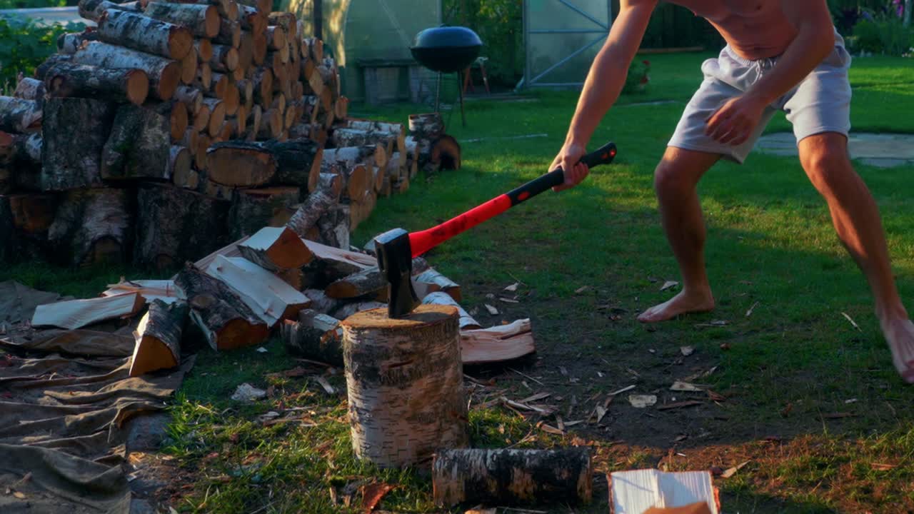 Strong Man Chopping Wood Using An Axe In The Backyard At Summer