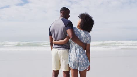 african american couple embracing and smiling at the beach