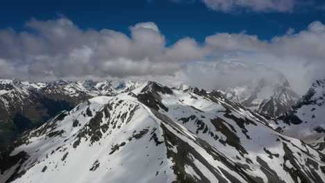 Air-flight-through-mountain-clouds-over-beautiful-snow-capped-peaks-of-mountains-and-glaciers.