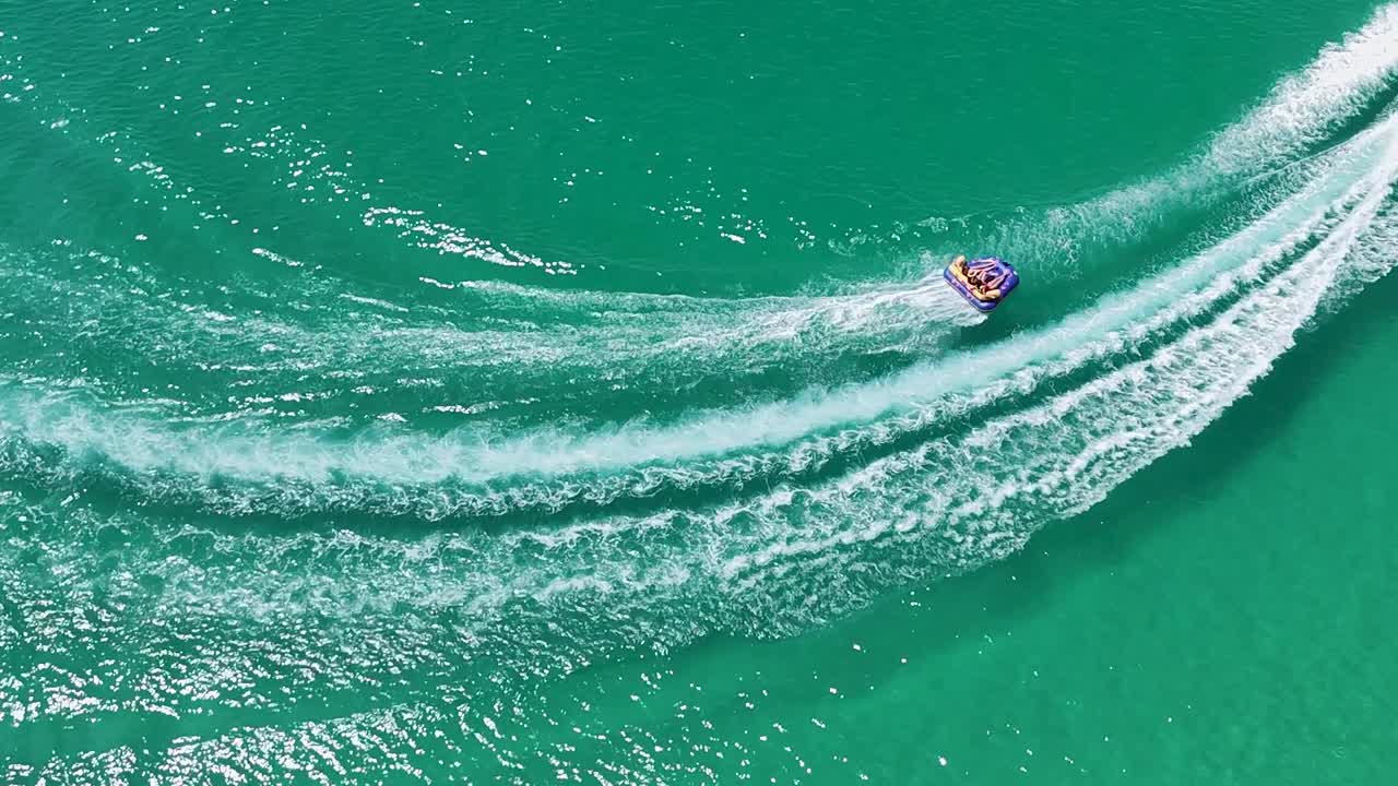 Drone captures a speedboat creating dynamic wake patterns on vibrant turquoise waters.