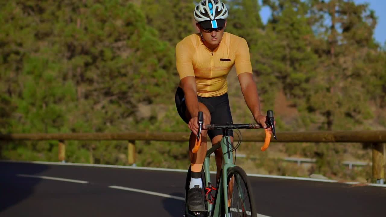 en este video de seguimiento, un ciclista masculino se enfrenta a una subida de carretera de montaña. se dedica al entrenamiento en bicicleta a lo largo de una carretera montañosa iluminada por el sol