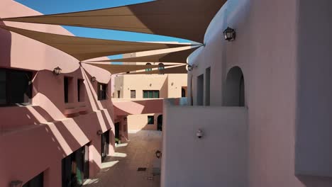 sunny courtyard with pink and white buildings and shade sails