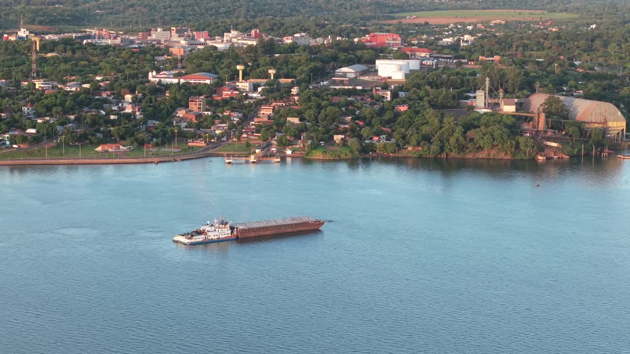 Aerial view of cargo barge sailing near urban riverfront, Paraguay international logistics