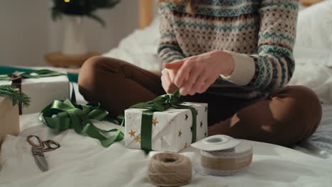 Unrecognizable-caucasian-woman-sitting-on-bed-and-packing-Christmas-gift-at-home