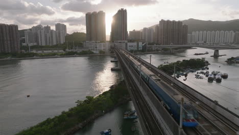 pull-away aerial shot of train passing over bridge from tsing yi island to ma wan, hong kong, with sun flares in the background