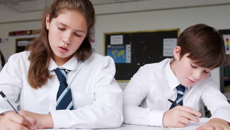 Male-And-Female-High-School-Students-Wearing-Uniform-Working-At-Desk-Together