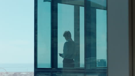 successful asian businessman using smartphone texting looking out window corporate executive sending emails on mobile phone working late managing company