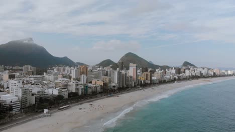 Movimiento-Panorámico-Aéreo-Que-Muestra-Los-Barrios-De-Playa-De-Leblon-E-Ipanema-Con-El-Corcovado-Y-La-Montaña-Del-Pan-De-Azúcar-Del-Paisaje-Urbano-De-Río-De-Janeiro-En-El-Fondo-Al-Atardecer-En-Un-Día-Nublado