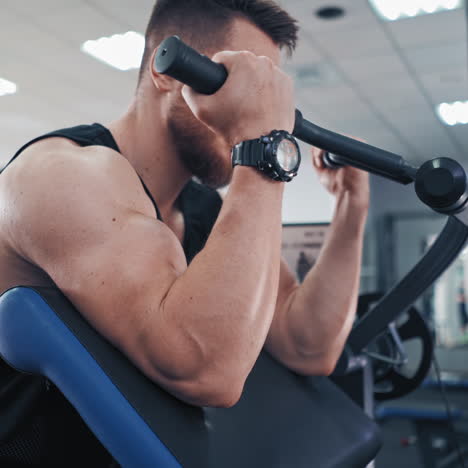 side view of an athletic man during workout in a gym. bodybuilder sitting in a modern simulator and trains his muscles of arms.