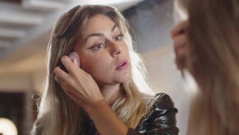 focused woman applying blush with brush while looking at mirror