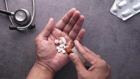 hand holding pills and a bottle of medication near a stethoscope