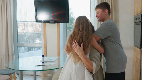 back view of kids in gray top and white gown approaching their mother in gray gown, both smiling and preparing to hug each other in cozy indoor setting, joyful family moment, love and warmth