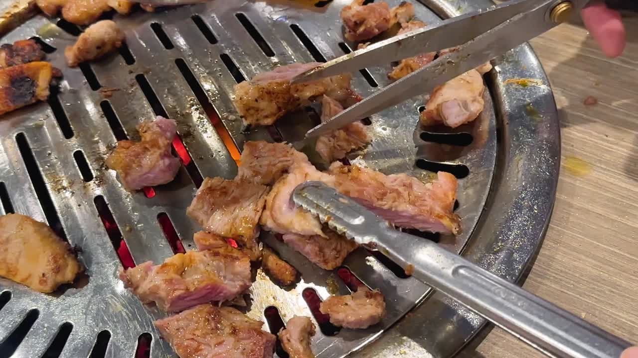 Tampilan jarak dekat tangan yang menggunakan penjepit logam dan gunting untuk memotong potongan daging babi yang mendesis.