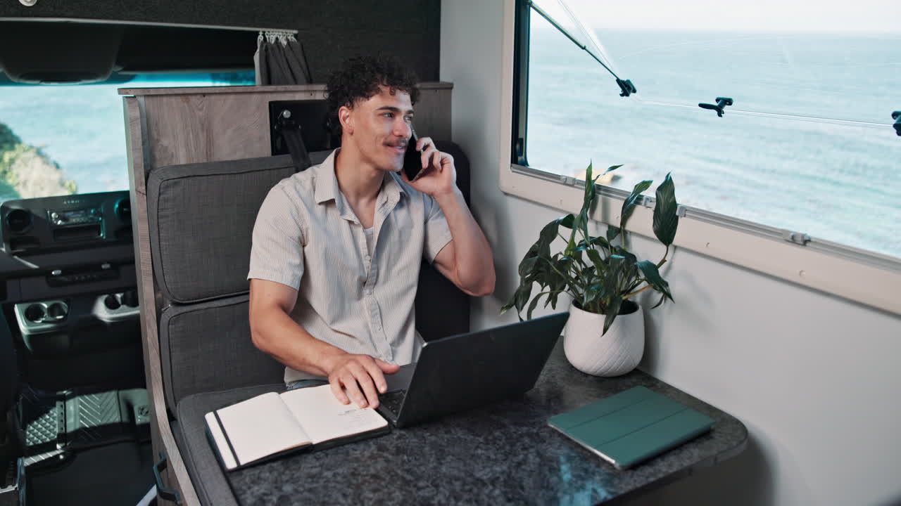 Young Man Talking on Phone and Working on Laptop in Camper Van