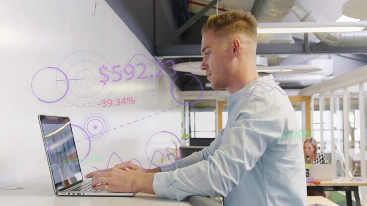 Woman reviewing proofs, glancing at charts, man walking up placing laptop, finance metrics on wall