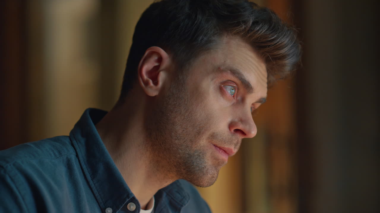 Closeup frowning guy overworking at evening flat. Serious man looking distance