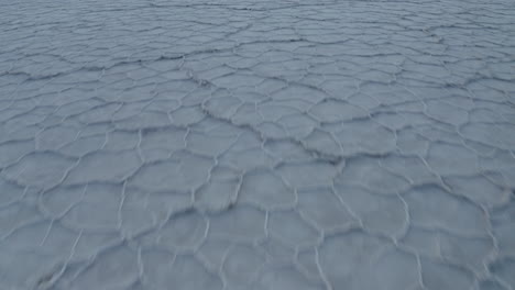 Drone-footage-flying-over-snd-panning-up-at-hexagonal-shapes-salt-flats-into-mountains-in-the-background,-Death-Valley-National-Park