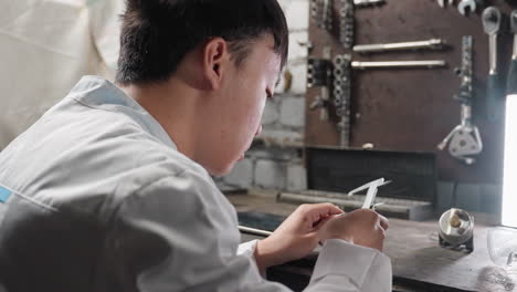 young engineer working with veiner caliper, adjusting and measuring diameter of boris in hand, in front of bright light, background features mechanical tools, workbench, and precision instruments