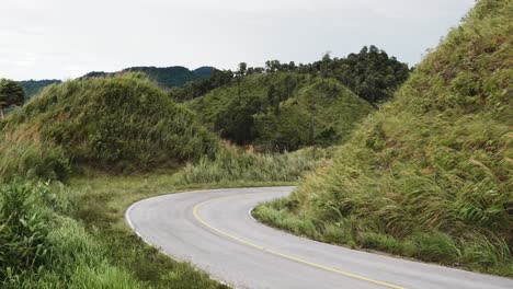 camino de curva vacío con colina de hierba alta y ventosa en el costado