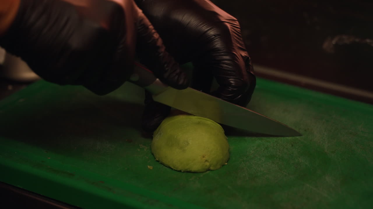 las manos del chef usando guantes de látex negro cortando avocado verde suave a mitad en la tabla de cortar