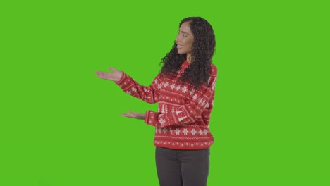 studio portrait of woman wearing christmas jumper showing item or object against green screen smiling at camera