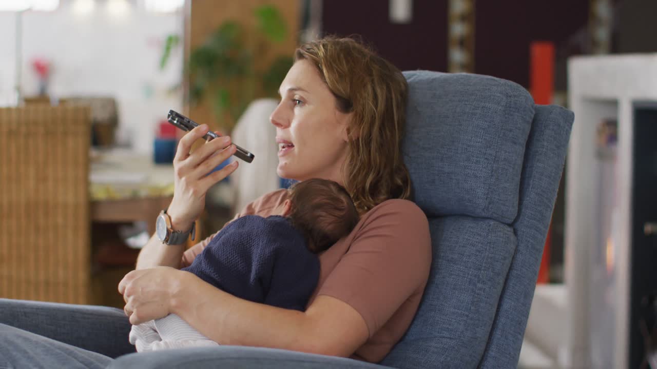 Video di madre caucasica seduta in poltrona con neonato e che usa lo smartphone