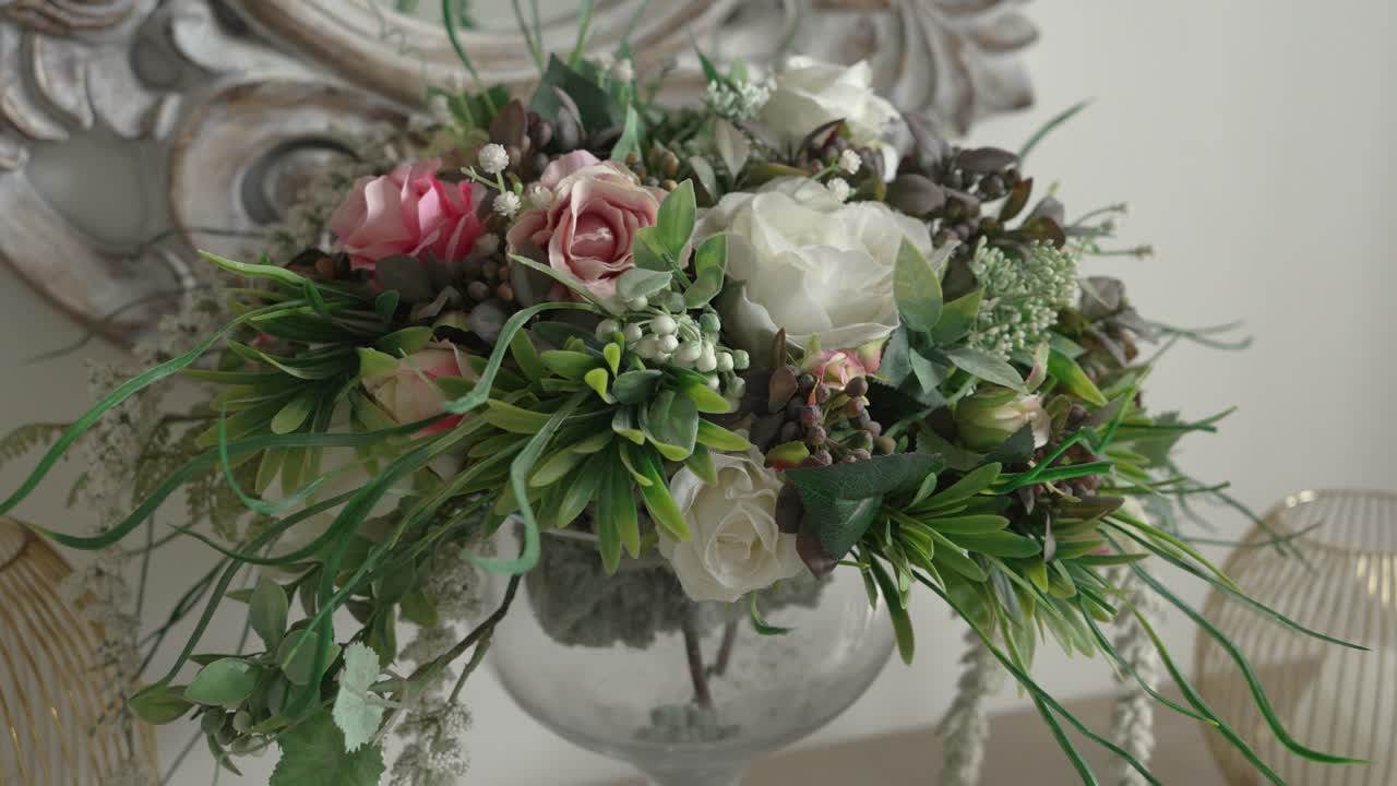 Una composizione floreale ben fatta è in un vaso di vetro accanto a uno specchio decorativo. I fiori aggiungono colore all'ambiente domestico. L'arredamento appare organizzato e invitante.