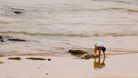 a child in colorful attire explores tidal pools on a sandy beach under soft daylight, capturing a moment of curiosity