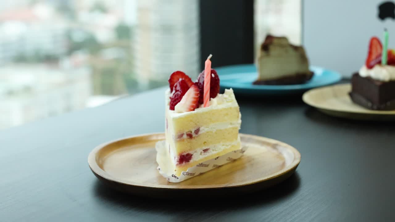Hand places candle on strawberry shortcake in daylight, cityscape background, and soft lighting