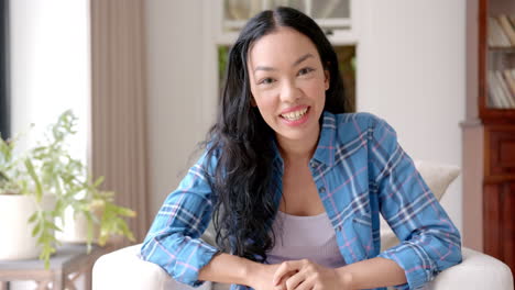 smiling asian woman sitting on couch on video call at home