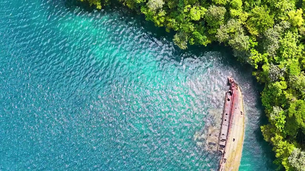 Ripresa aerea con drone di un relitto arrugginito che riposa vicino a un'isola tropicale lussureggiante.