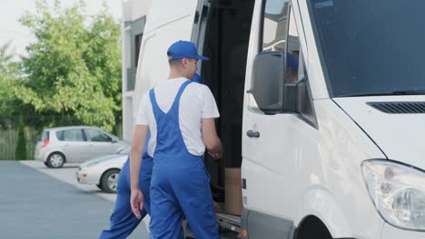 two young workers of removal company are loading boxes and furniture into a minibus