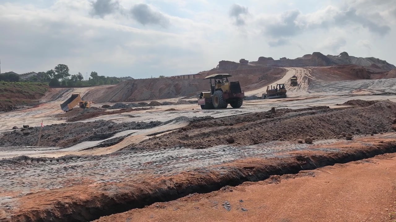 Heavy machinery performs earthworks on a hilly terrain. The slope is being leveled to create a flat platform. This foundation will be used for future residential housing construction.