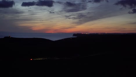 two cars drive through countryside with golden sunset and sea in the distance