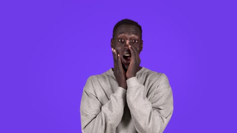 young short haired afro american man in white stylish shirt on blue background. talking, male holds hand to his mouth and speaks, whispering. the concept of chatter, gossip, talk