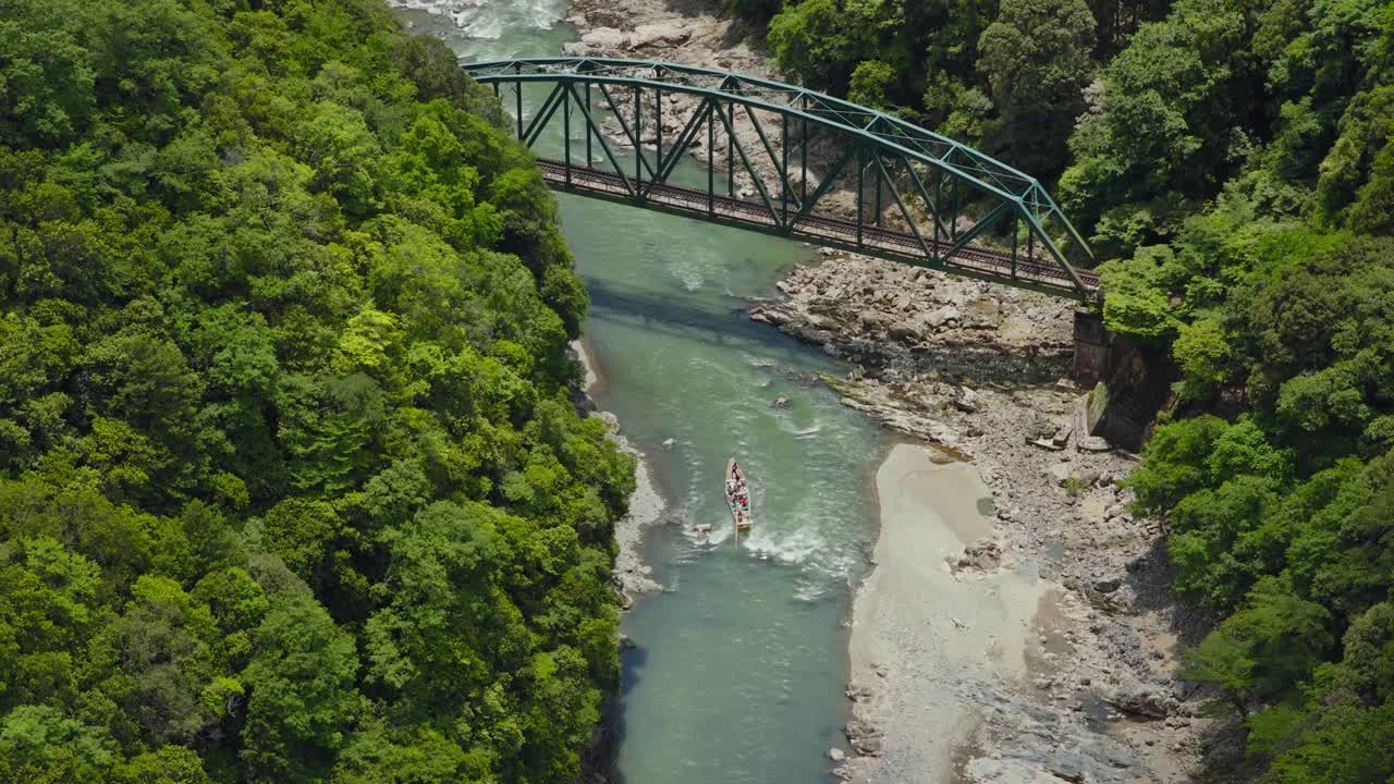 Aerial view of boat sailing under train bridge on Hozugawa River Kyoto Japan