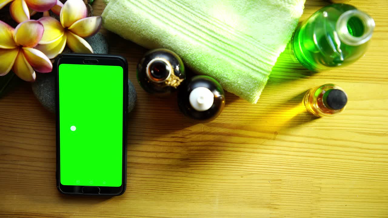 나무 배경에 프랑기파니, 수건 및 마사지 기름에 대항하여 녹색 화면 스마트 폰을 들고 있는 남자