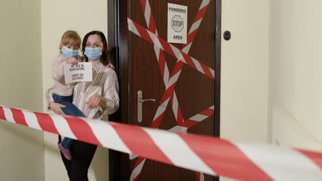 sick mother with kid daughter in medical masks opening home door, coronavirus quarantine lockdown