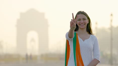 Happy-Indian-girl-showing-Victory-sign-at-India-gate-in-an-Indian-wear