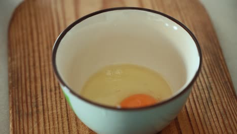 a close up shot of a breaking raw egg into a white bowl, brown wooden plate, 4k video