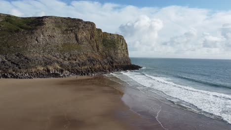 aerial rising shot on sandy mewslade beach with coastal cliff with layers of rock visible in gower peninsula wales uk 4k