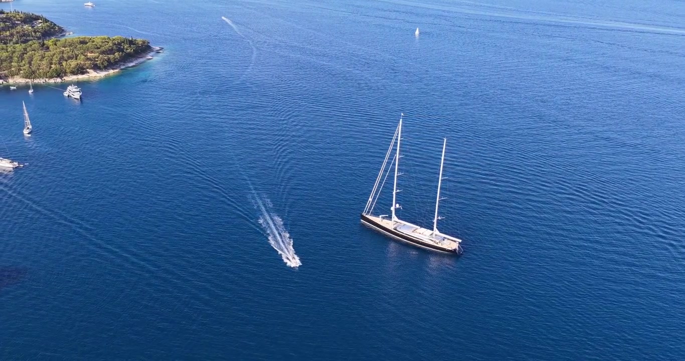 Vista aerea di un grande superyacht di lusso e di un piccolo motoscafo che navigano nel profondo Mar Ionio blu vicino alla costa di Kerasia, Corfù, Grecia. Video stock estivo